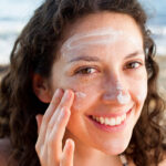 Smiling woman applying sunscreen to face